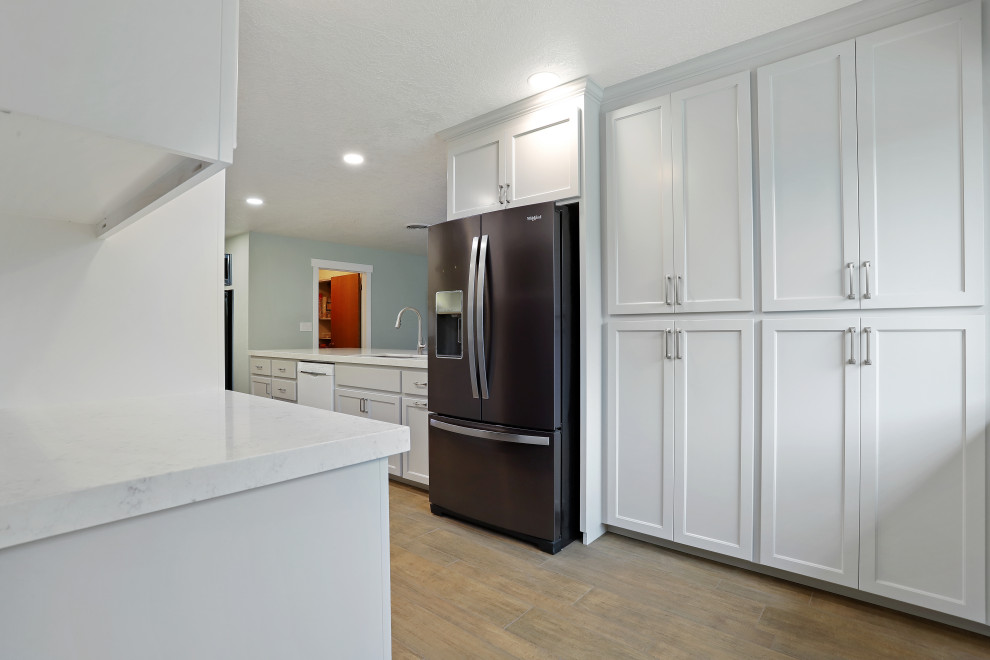 Foto på ett funkis vit kök, med en undermonterad diskho, vita skåp, bänkskiva i kvarts, grått stänkskydd, stänkskydd i glaskakel, rostfria vitvaror, klinkergolv i porslin och brunt golv