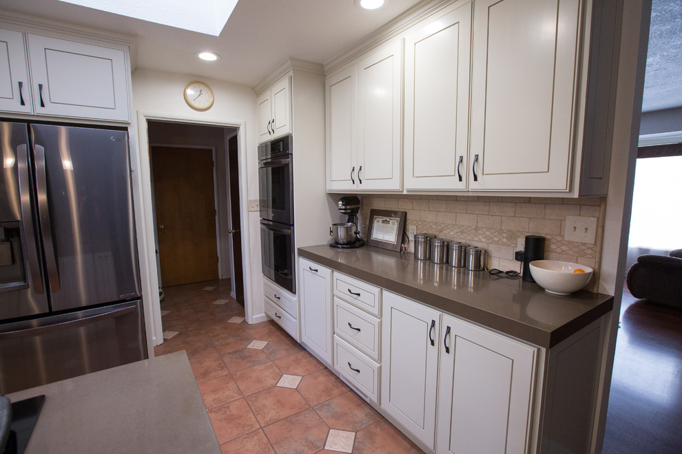 Foto di una cucina minimalista con lavello sottopiano, ante bianche, top in pietra calcarea, paraspruzzi beige e elettrodomestici in acciaio inossidabile