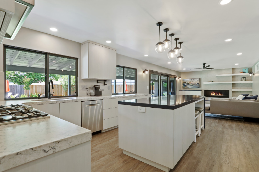 Inredning av ett modernt vit vitt kök, med en undermonterad diskho, vita skåp, bänkskiva i kvarts, grått stänkskydd, stänkskydd i porslinskakel, rostfria vitvaror, laminatgolv, en köksö och brunt golv