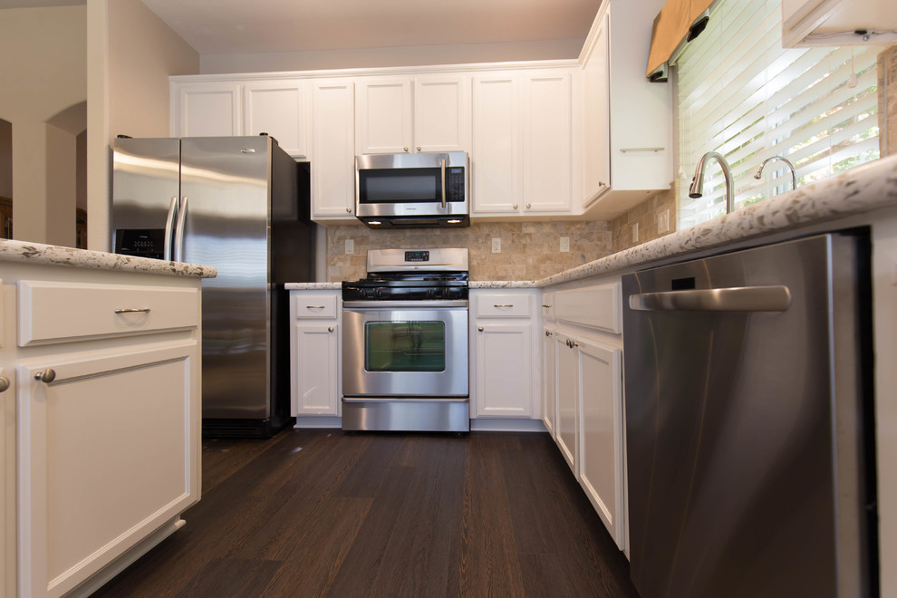 Modern inredning av ett kök, med en undermonterad diskho, vita skåp, bänkskiva i kvarts, beige stänkskydd, stänkskydd i travertin, rostfria vitvaror och en köksö
