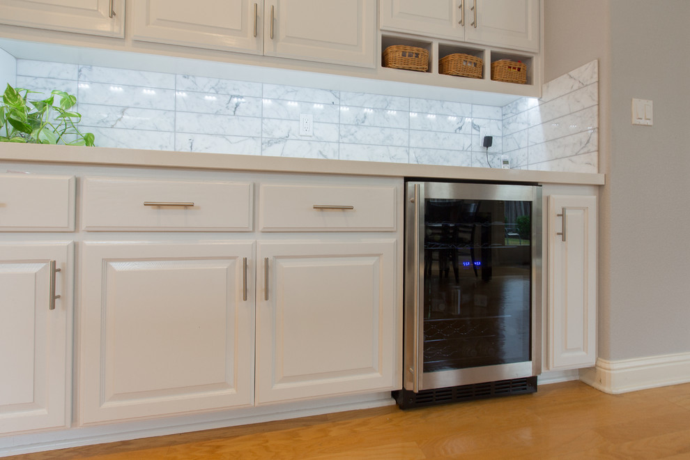 Foto på ett funkis u-kök, med en undermonterad diskho, vita skåp, bänkskiva i kvarts, vitt stänkskydd, stänkskydd i keramik och en halv köksö