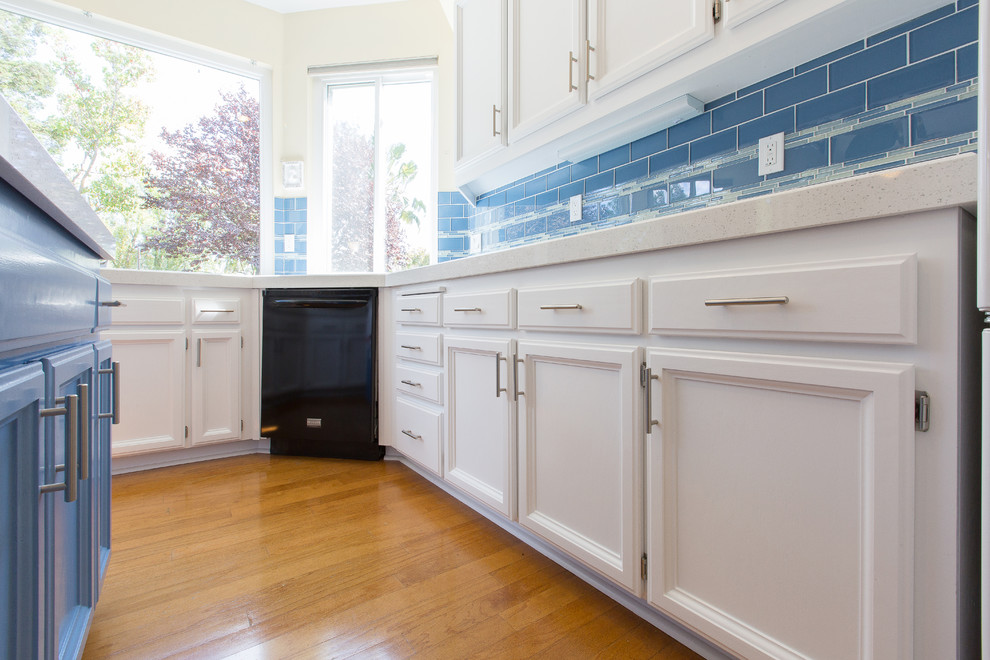 Cette image montre une cuisine minimaliste en U avec un évier encastré, des portes de placard blanches, un plan de travail en quartz modifié et une crédence bleue.