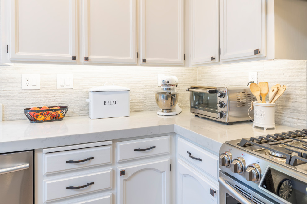 This is an example of a contemporary l-shaped kitchen/diner in San Francisco with a belfast sink, white cabinets, engineered stone countertops, beige splashback, porcelain splashback, stainless steel appliances, an island and white worktops.