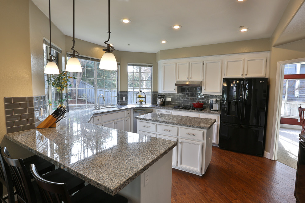 Example of a classic u-shaped eat-in kitchen design in Dublin with an undermount sink, white cabinets, granite countertops, gray backsplash and glass tile backsplash