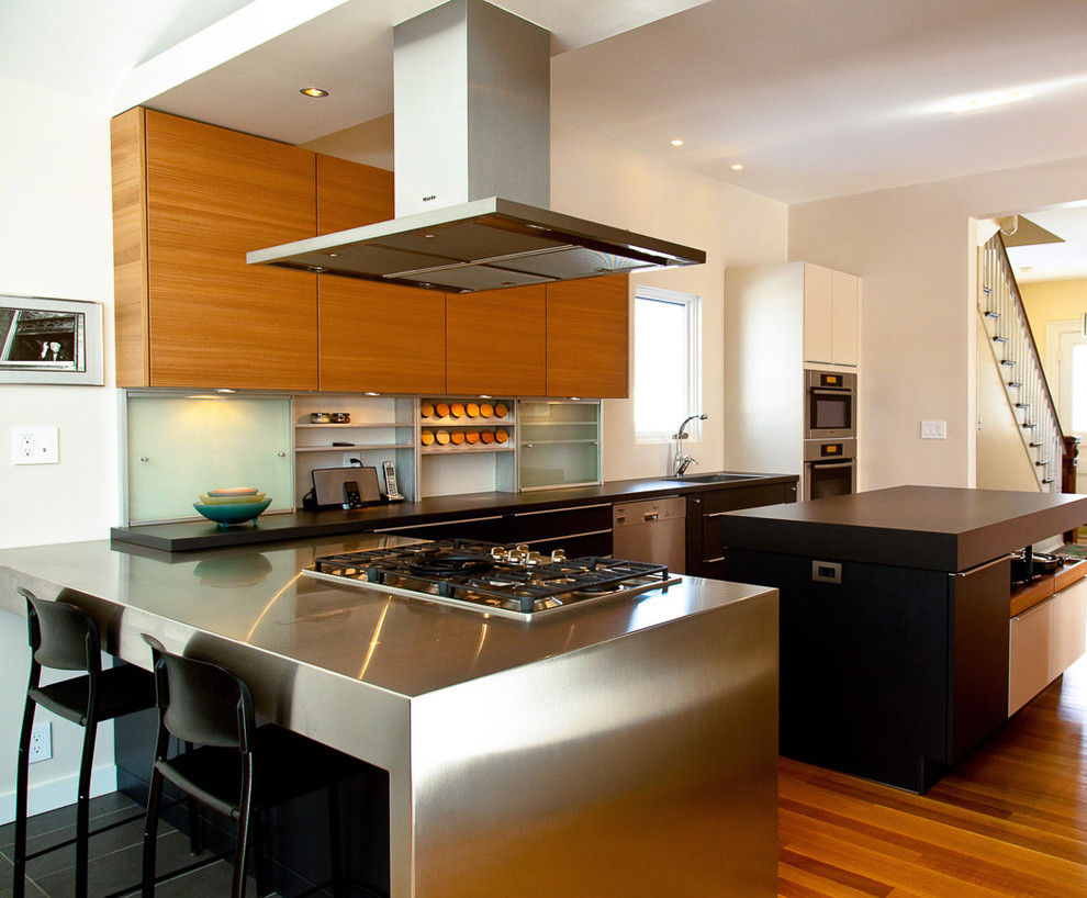Cette photo montre une cuisine tendance en bois brun et L avec un placard à porte plane, un plan de travail en inox et un électroménager en acier inoxydable.
