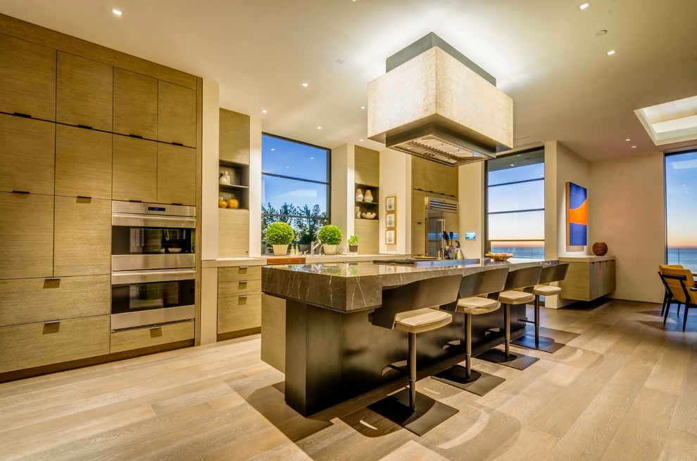 Zweizeilige Moderne Küche mit flächenbündigen Schrankfronten, hellbraunen Holzschränken, Küchengeräten aus Edelstahl, hellem Holzboden und Kücheninsel in San Diego