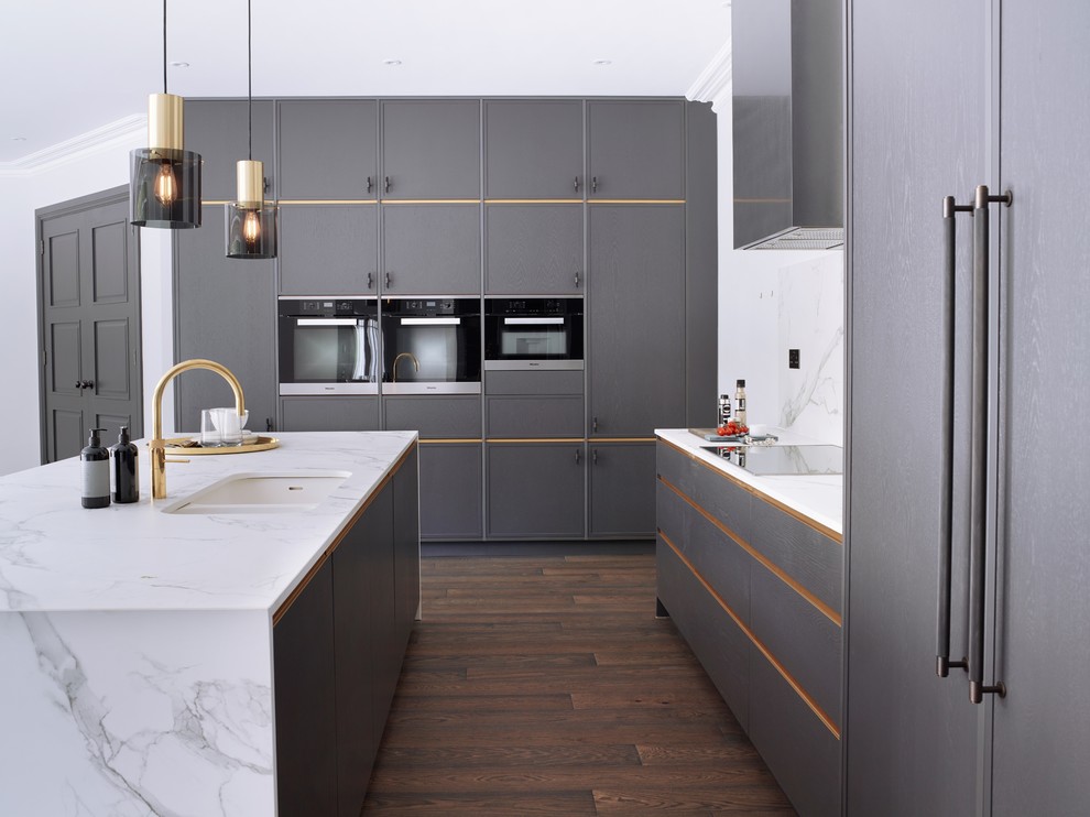 Foto på ett mellanstort funkis vit l-kök, med en köksö, en dubbel diskho, släta luckor, grå skåp, vitt stänkskydd, svarta vitvaror, mörkt trägolv, brunt golv och marmorbänkskiva