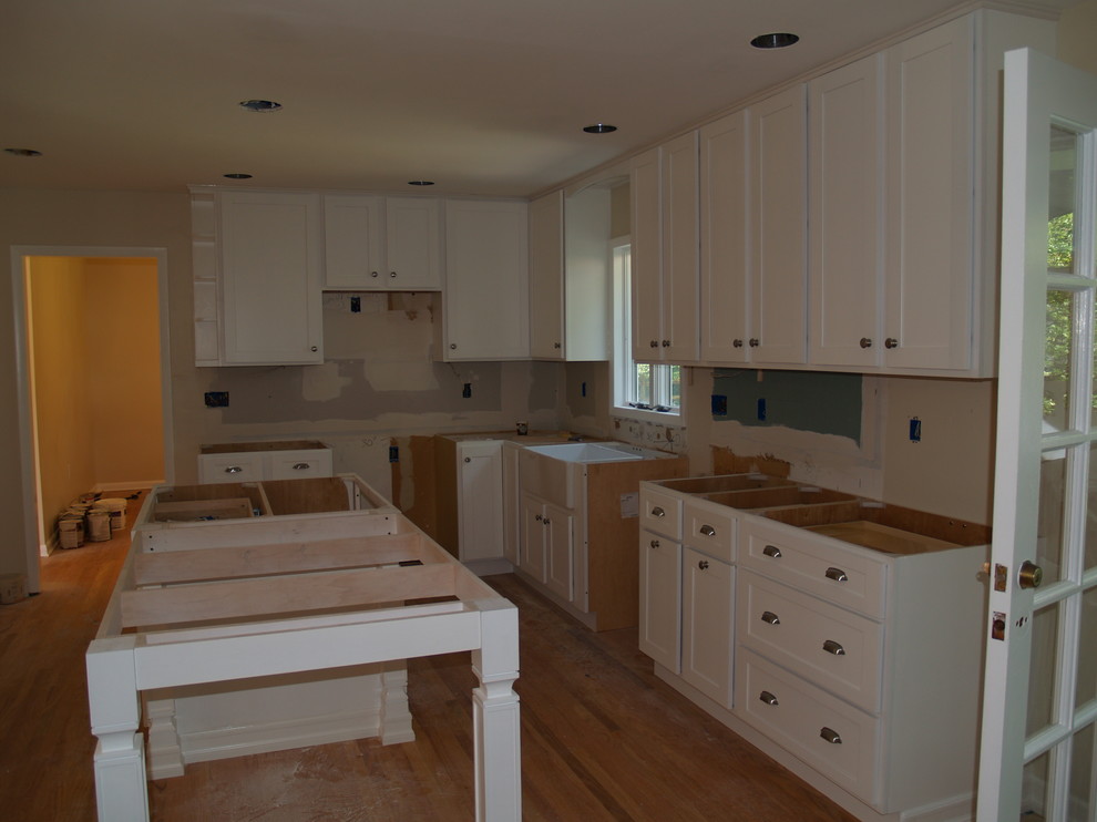 Large contemporary galley kitchen/diner in New York with a belfast sink, flat-panel cabinets, white cabinets, laminate countertops, stainless steel appliances, light hardwood flooring and an island.