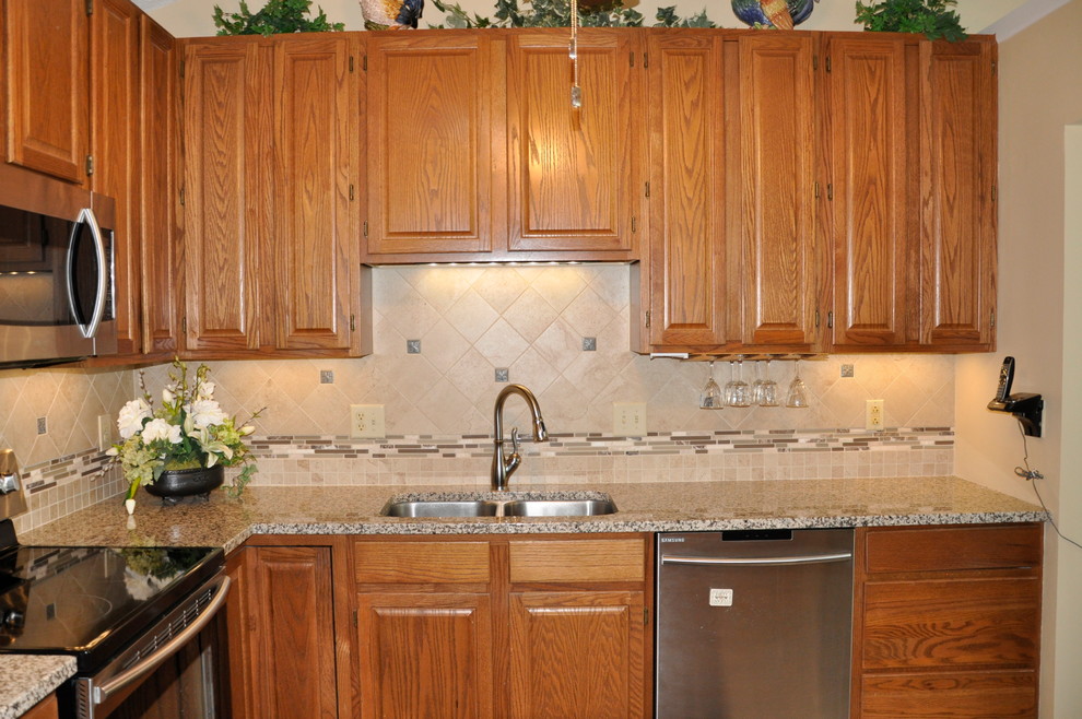Klassisk inredning av ett avskilt, litet u-kök, med en undermonterad diskho, luckor med infälld panel, skåp i mellenmörkt trä, granitbänkskiva, beige stänkskydd, stänkskydd i stenkakel, rostfria vitvaror och linoleumgolv