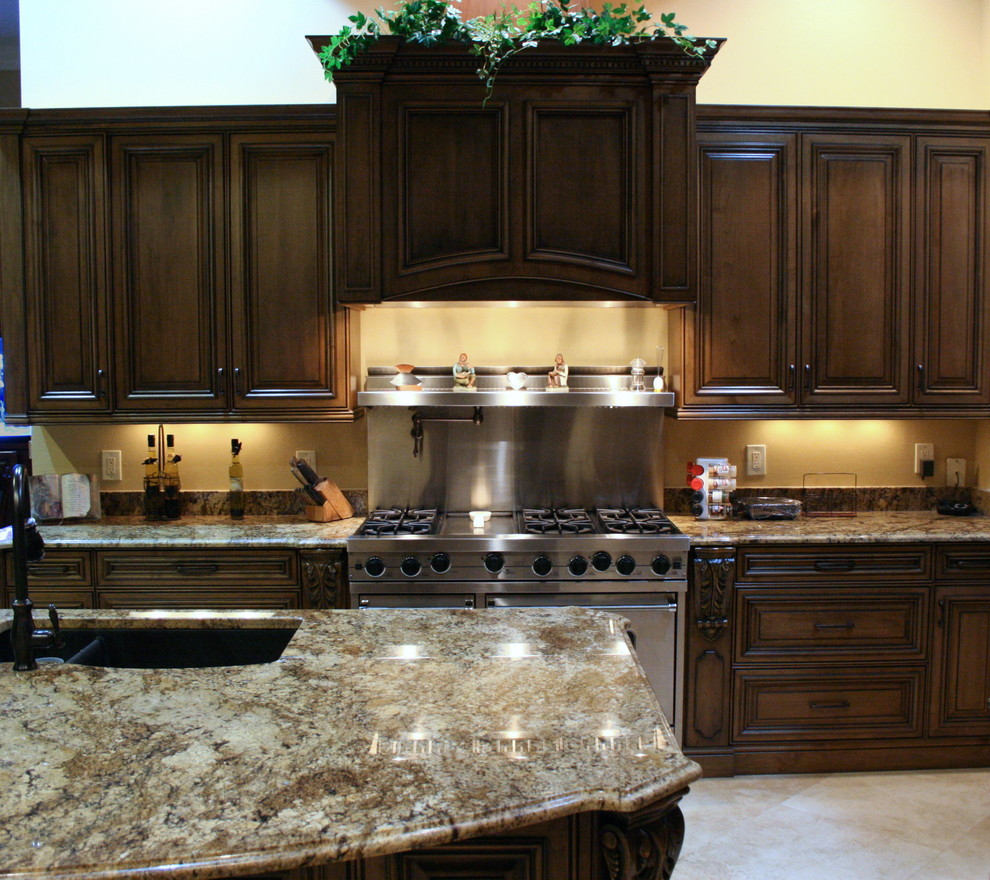Immagine di una cucina minimal di medie dimensioni con lavello sottopiano, ante con bugna sagomata, ante in legno scuro, top in granito e elettrodomestici in acciaio inossidabile