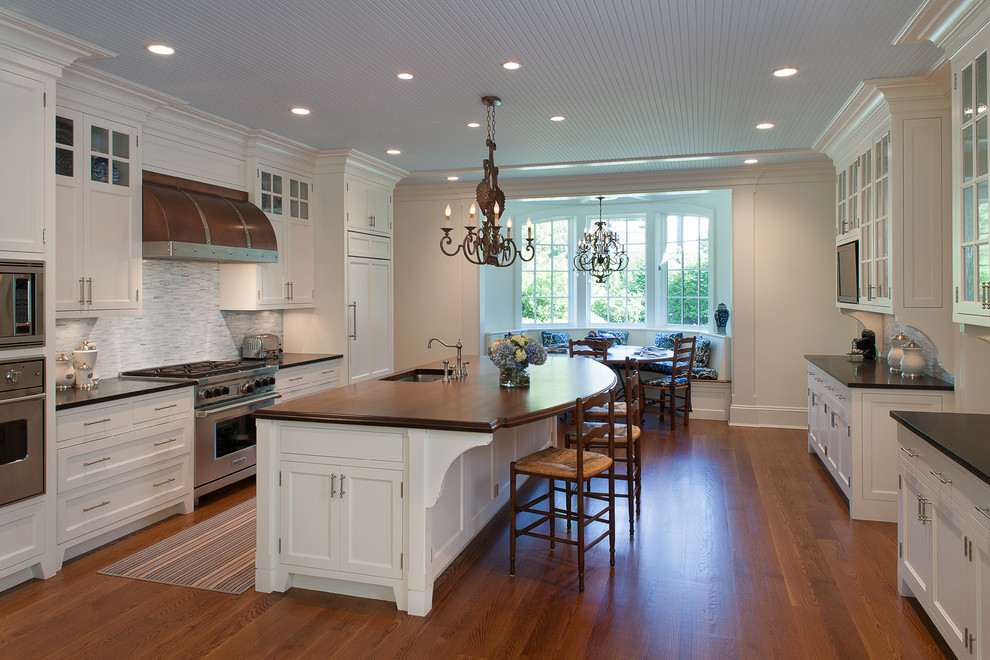 Inspiration for a timeless galley medium tone wood floor and brown floor eat-in kitchen remodel in New York with an undermount sink, recessed-panel cabinets, white cabinets, wood countertops, blue backsplash, stainless steel appliances, an island and brown countertops