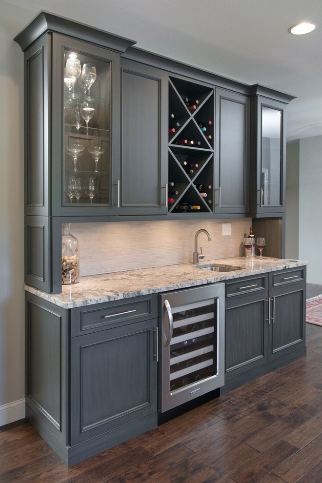 This is an example of a large country l-shaped home bar in Kansas City with recessed-panel cabinets, beige cabinets, granite worktops, beige splashback and dark hardwood flooring.