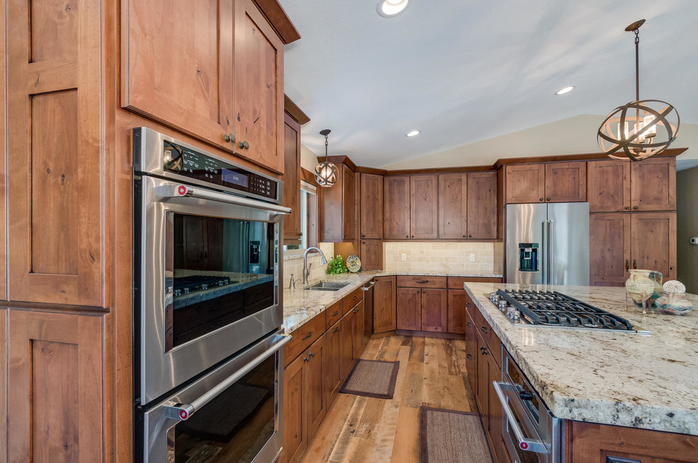 Photo of a large rustic l-shaped enclosed kitchen in Denver with a submerged sink, shaker cabinets, medium wood cabinets, granite worktops, beige splashback, stone tiled splashback, stainless steel appliances, medium hardwood flooring, an island and brown floors.