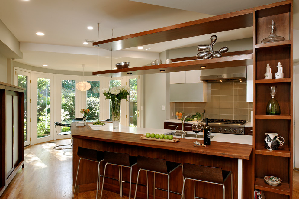Klassisk inredning av ett kök och matrum, med en undermonterad diskho, släta luckor, skåp i mörkt trä, brunt stänkskydd, rostfria vitvaror och stänkskydd i glaskakel