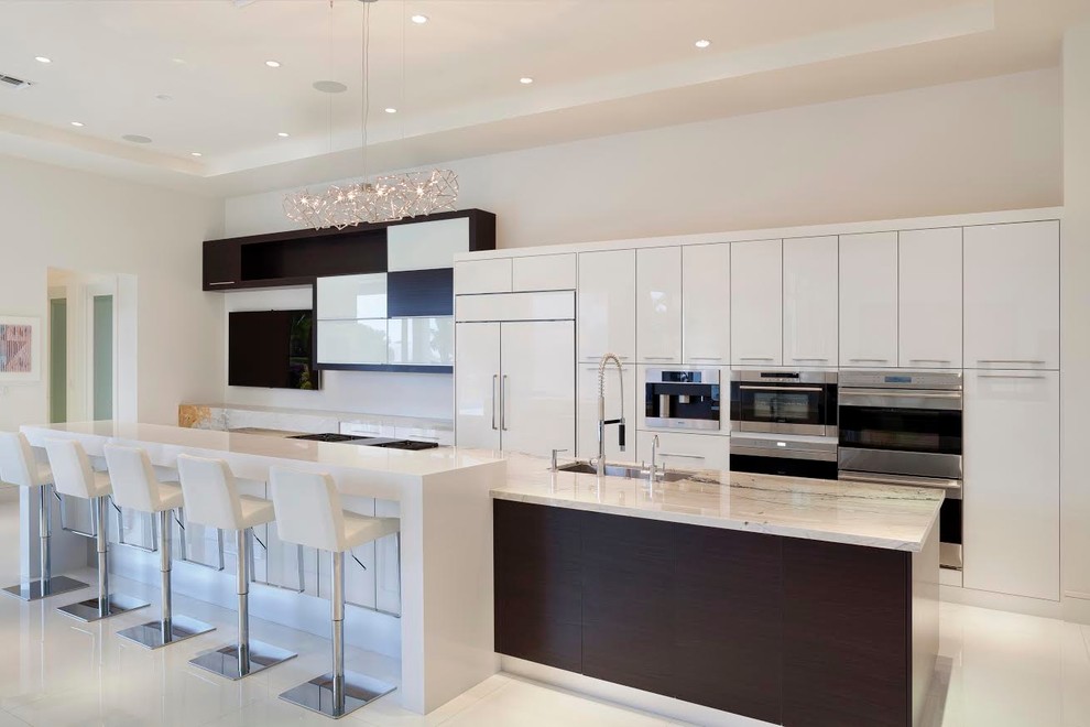 This is an example of an expansive modern single-wall open plan kitchen in Miami with a submerged sink, flat-panel cabinets, white cabinets, marble worktops, stainless steel appliances, marble flooring and an island.
