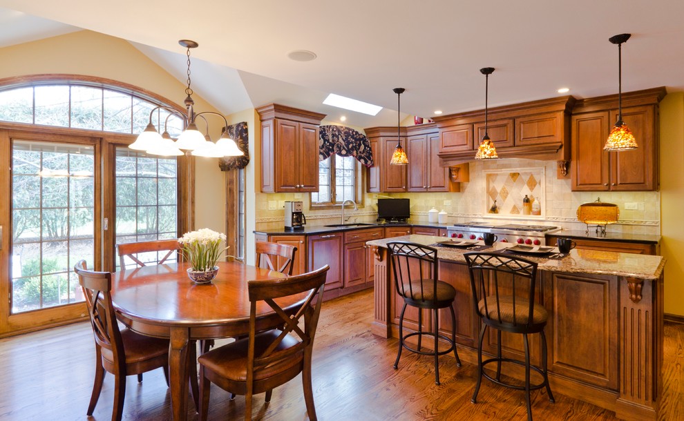 Example of a classic l-shaped eat-in kitchen design in Chicago with a drop-in sink, raised-panel cabinets, medium tone wood cabinets, granite countertops, beige backsplash, ceramic backsplash and stainless steel appliances