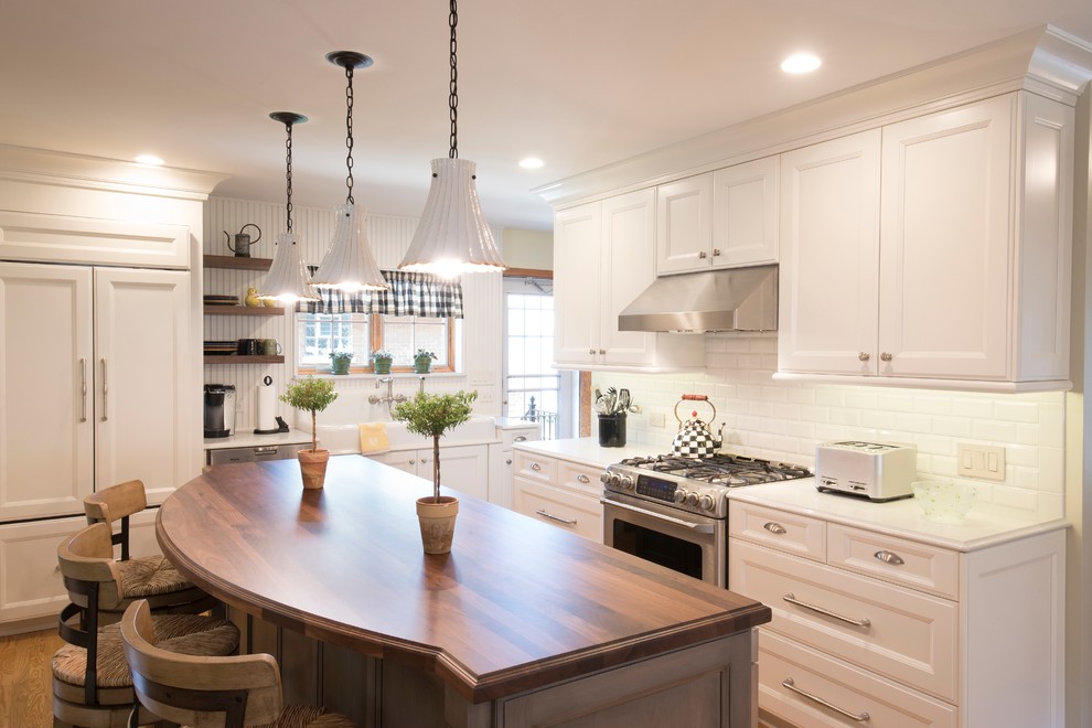 Example of a mid-sized farmhouse l-shaped light wood floor and beige floor eat-in kitchen design in Chicago with a farmhouse sink, recessed-panel cabinets, wood countertops, white backsplash, subway tile backsplash, stainless steel appliances, an island and brown countertops