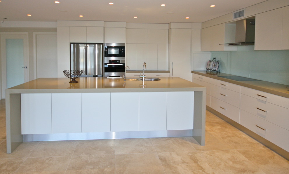 Large contemporary l-shaped open plan kitchen in Sydney with a submerged sink, flat-panel cabinets, white cabinets, engineered stone countertops, glass sheet splashback, stainless steel appliances, ceramic flooring, an island and blue splashback.
