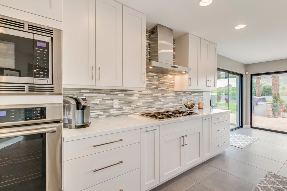 Inredning av ett modernt mellanstort vit vitt kök, med en undermonterad diskho, skåp i shakerstil, vita skåp, bänkskiva i kvarts, grått stänkskydd, stänkskydd i mosaik, rostfria vitvaror, klinkergolv i porslin, en köksö och grått golv