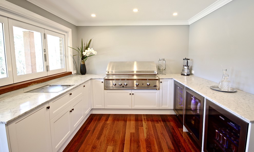 This is an example of a large classic u-shaped open plan kitchen in Sydney with a double-bowl sink, recessed-panel cabinets, white cabinets, marble worktops, grey splashback, glass sheet splashback, stainless steel appliances, medium hardwood flooring and no island.