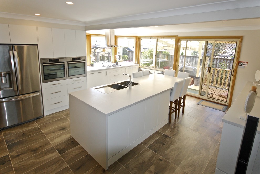 Large galley ceramic tile enclosed kitchen photo in Sydney with a drop-in sink, flat-panel cabinets, white cabinets, quartz countertops, glass sheet backsplash, stainless steel appliances and an island