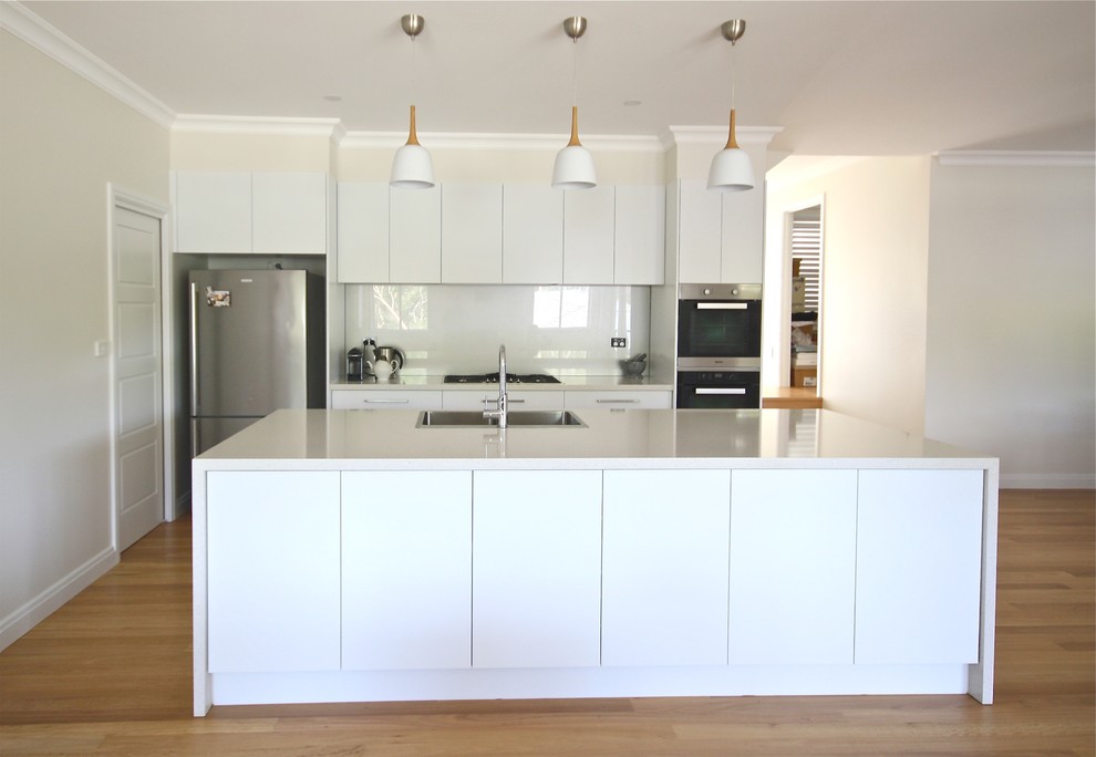 Example of a mid-sized minimalist single-wall light wood floor eat-in kitchen design in Sydney with a double-bowl sink, flat-panel cabinets, white cabinets, quartz countertops, beige backsplash, stone slab backsplash, stainless steel appliances and an island