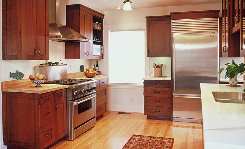 Bild på ett stort vintage kök, med en undermonterad diskho, luckor med infälld panel, skåp i mörkt trä, träbänkskiva, rostfria vitvaror och mellanmörkt trägolv