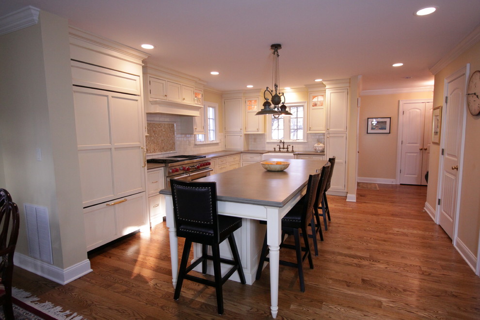 Example of a mid-sized classic galley medium tone wood floor eat-in kitchen design in New York with a farmhouse sink, beaded inset cabinets, white cabinets, concrete countertops, white backsplash, ceramic backsplash, stainless steel appliances and an island