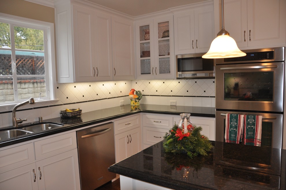 Exempel på ett klassiskt kök, med en undermonterad diskho, vita skåp, granitbänkskiva, vitt stänkskydd, stänkskydd i keramik, rostfria vitvaror och en köksö