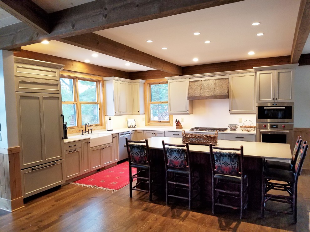 Foto på ett amerikanskt kök, med en rustik diskho, luckor med infälld panel, vita skåp, vitt stänkskydd, integrerade vitvaror, mellanmörkt trägolv och en köksö