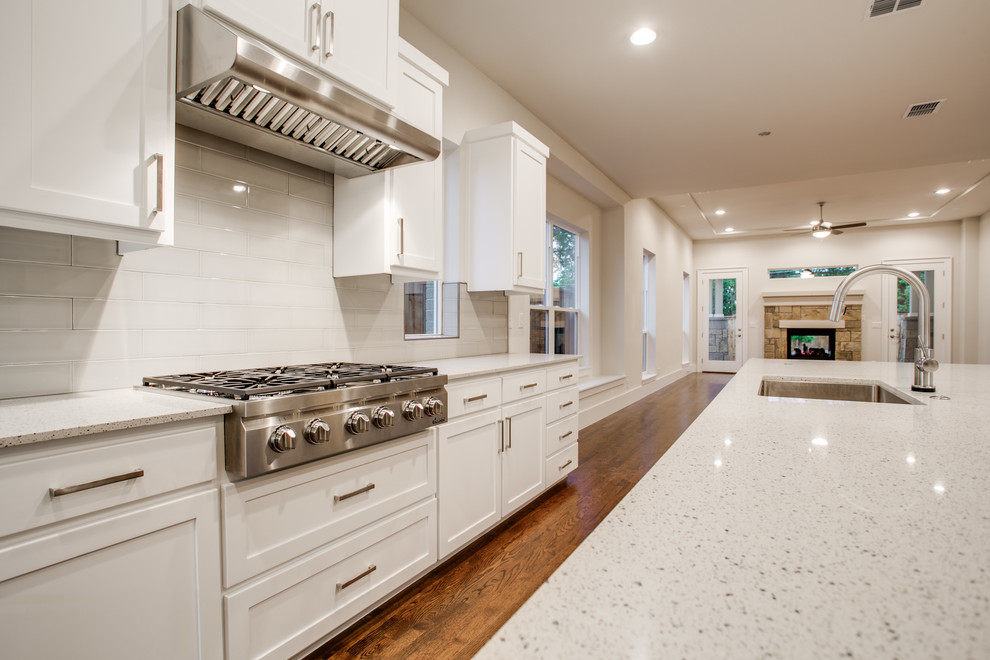 Eat-in kitchen - large traditional l-shaped medium tone wood floor eat-in kitchen idea in Dallas with a farmhouse sink, shaker cabinets, white cabinets, quartzite countertops, white backsplash, stainless steel appliances and an island