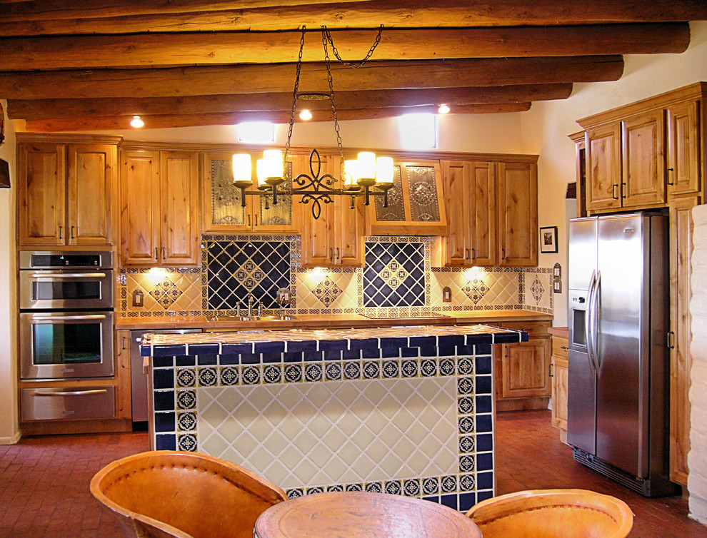 Idée de décoration pour une cuisine ouverte linéaire sud-ouest américain en bois brun de taille moyenne avec un évier posé, un placard avec porte à panneau surélevé, une crédence bleue, une crédence en céramique, un électroménager en acier inoxydable, un sol en brique, îlot et un sol rouge.