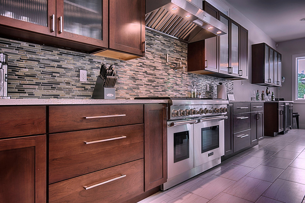 Example of a mid-sized classic l-shaped porcelain tile eat-in kitchen design in New Orleans with shaker cabinets, stainless steel appliances, an island, medium tone wood cabinets, granite countertops, multicolored backsplash and matchstick tile backsplash