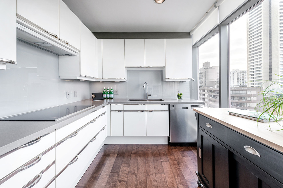 Example of a trendy l-shaped light wood floor enclosed kitchen design in Vancouver with white cabinets, gray backsplash, stainless steel appliances, a double-bowl sink, flat-panel cabinets and an island