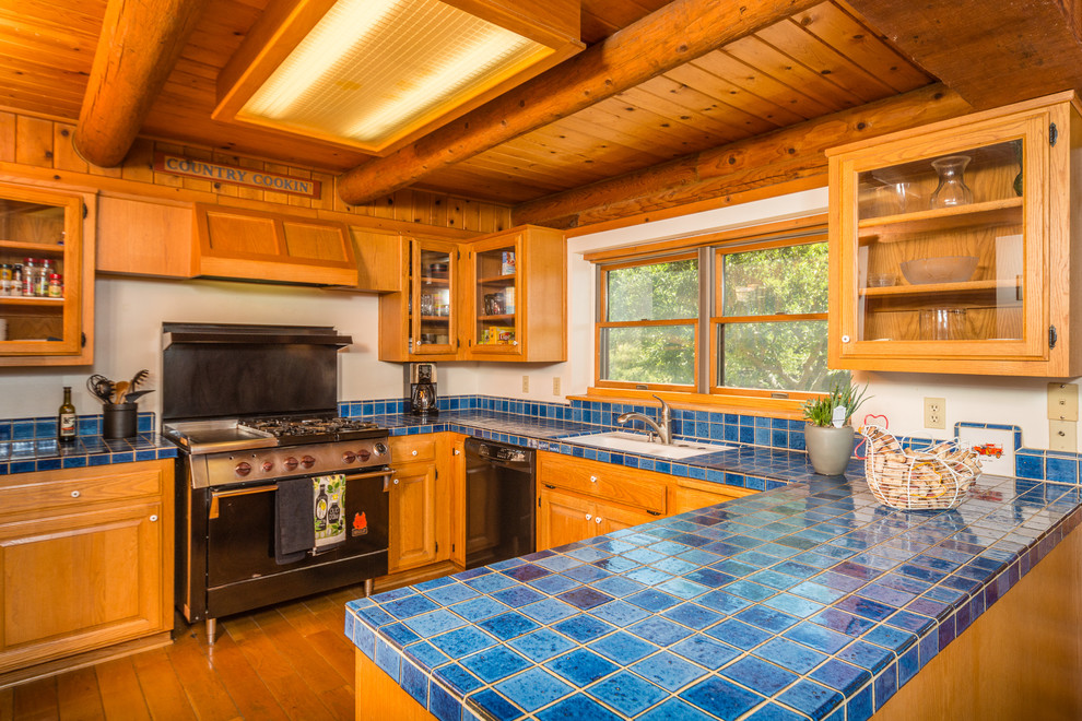 サンルイスオビスポにあるカントリー風のおしゃれなキッチン (レイズドパネル扉のキャビネット、中間色木目調キャビネット、黒い調理設備、タイルカウンター) の写真