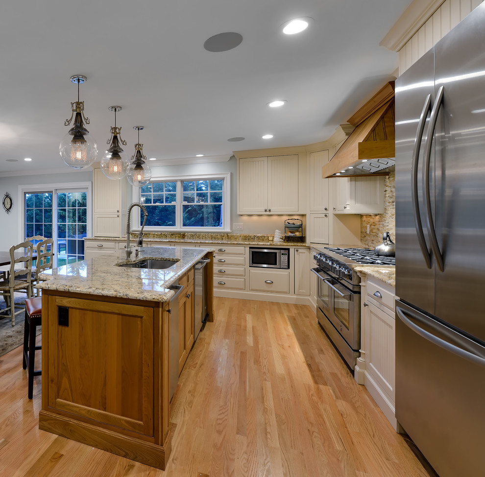 Example of a beach style light wood floor kitchen design in New York with an undermount sink, recessed-panel cabinets, beige cabinets, granite countertops, multicolored backsplash, matchstick tile backsplash and stainless steel appliances