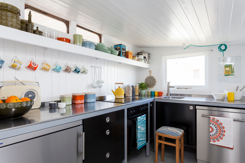Modelo de cocinas en L escandinava con fregadero integrado, armarios con paneles lisos, puertas de armario negras, encimera de acero inoxidable, salpicadero blanco y electrodomésticos de acero inoxidable