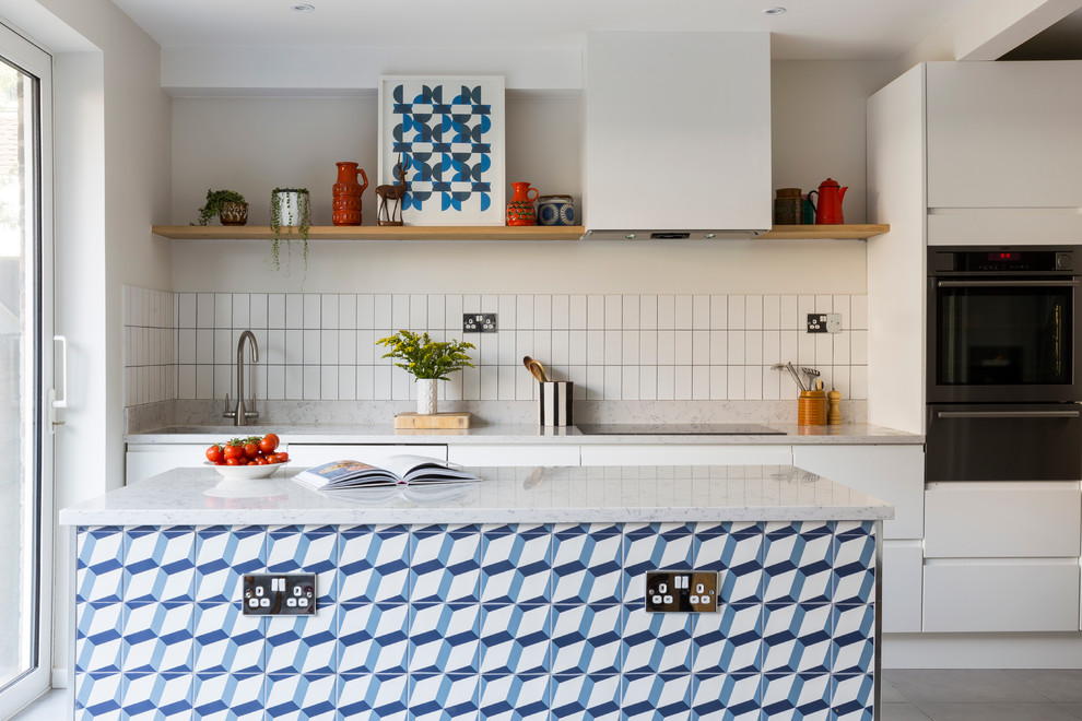 Cette image montre une cuisine parallèle design avec un évier encastré, un placard à porte plane, des portes de placard blanches, une crédence blanche, un électroménager en acier inoxydable et îlot.