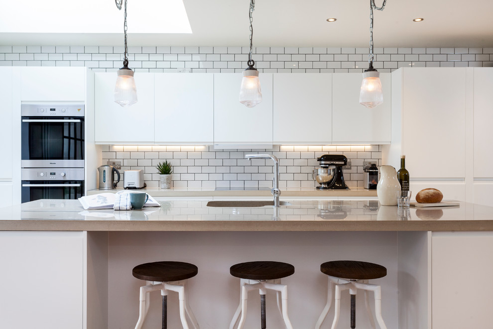 Design ideas for a traditional galley kitchen in London with an integrated sink, flat-panel cabinets, white cabinets, white splashback, metro tiled splashback and an island.