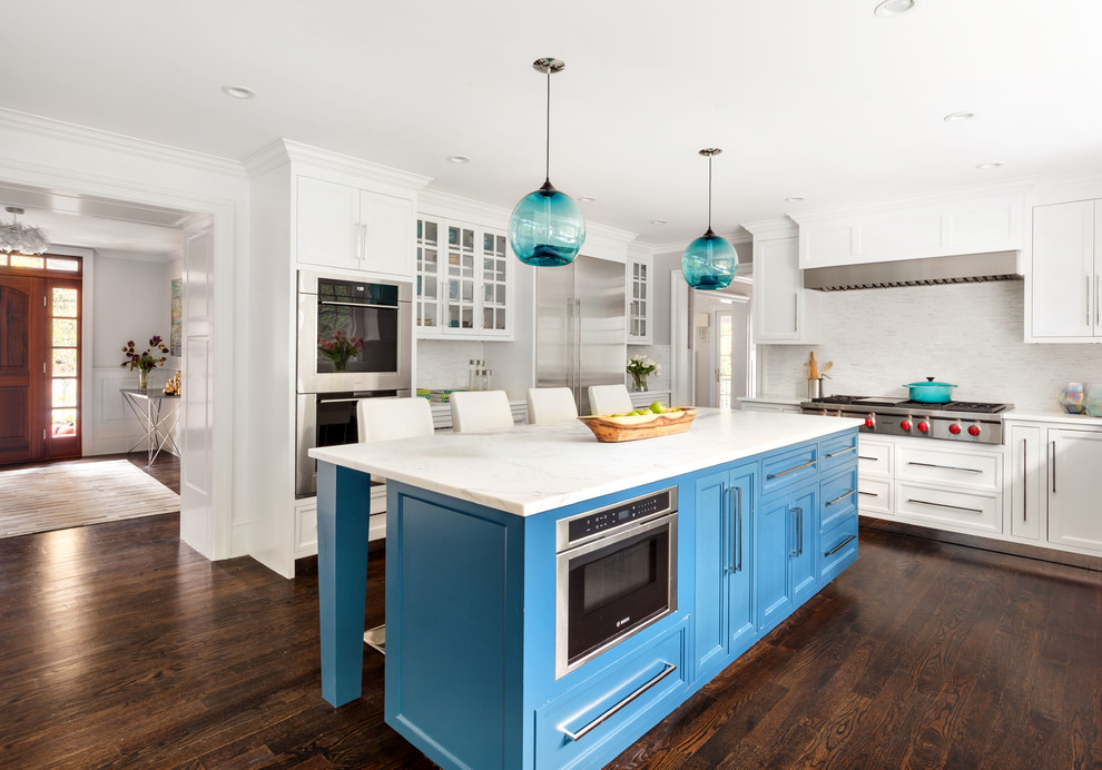 Klassisk inredning av ett kök, med skåp i shakerstil, blå skåp, vitt stänkskydd, rostfria vitvaror, mörkt trägolv, en köksö och brunt golv