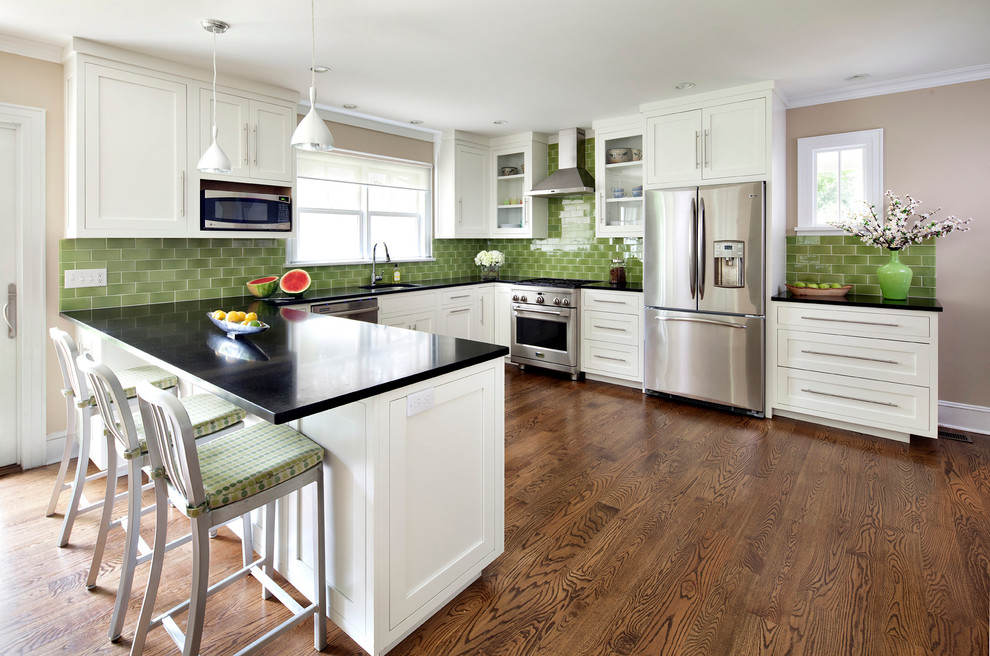Bild på ett kök, med rostfria vitvaror, en undermonterad diskho, skåp i shakerstil, vita skåp, granitbänkskiva, grönt stänkskydd och stänkskydd i keramik