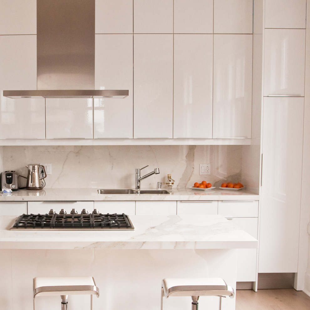Modern inredning av ett mellanstort kök, med en undermonterad diskho, släta luckor, vita skåp, marmorbänkskiva, vitt stänkskydd, stänkskydd i sten, rostfria vitvaror, ljust trägolv och en halv köksö