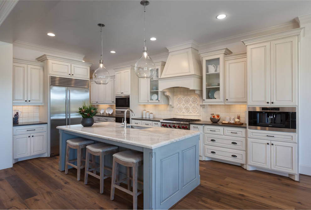 Inspiration for a large traditional l-shaped open plan kitchen in Houston with a built-in sink, raised-panel cabinets, white cabinets, granite worktops, white splashback, mosaic tiled splashback, stainless steel appliances, light hardwood flooring and an island.