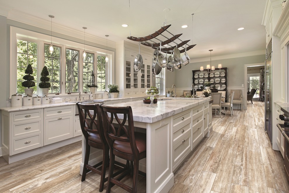 Eat-in kitchen - large traditional galley porcelain tile eat-in kitchen idea in Denver with a farmhouse sink, recessed-panel cabinets, white cabinets, marble countertops, stainless steel appliances and an island