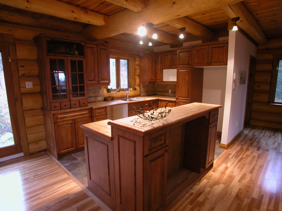 Foto på ett mellanstort rustikt l-kök, med en nedsänkt diskho, luckor med upphöjd panel, skåp i mellenmörkt trä, beige stänkskydd, stänkskydd i keramik, ljust trägolv och en köksö