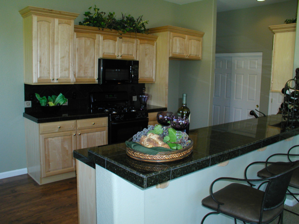 Example of a mid-sized classic galley dark wood floor and brown floor eat-in kitchen design in Other with a double-bowl sink, raised-panel cabinets, light wood cabinets, granite countertops, black backsplash, stone slab backsplash, black appliances and an island