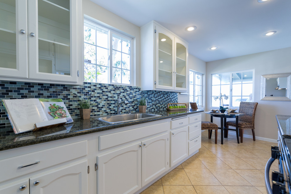 Photo of a traditional galley kitchen/diner in Los Angeles with a single-bowl sink, glass-front cabinets, white cabinets, granite worktops, blue splashback, metro tiled splashback and ceramic flooring.
