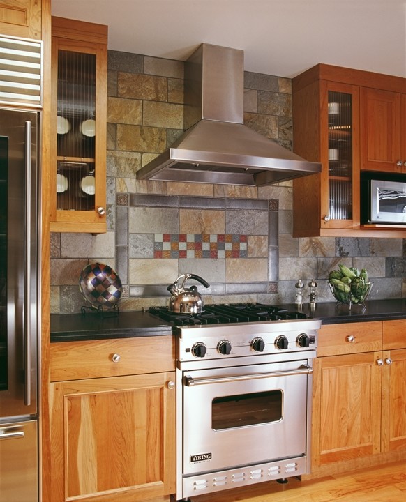 Imagen de cocina de estilo americano con armarios estilo shaker, puertas de armario de madera oscura, encimera de granito, salpicadero verde, salpicadero de azulejos de piedra y electrodomésticos de acero inoxidable