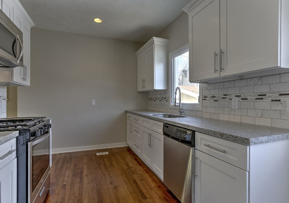 Inspiration for a small classic galley kitchen/diner in Omaha with a submerged sink, shaker cabinets, white cabinets, granite worktops, white splashback, stone tiled splashback, stainless steel appliances, medium hardwood flooring and no island.