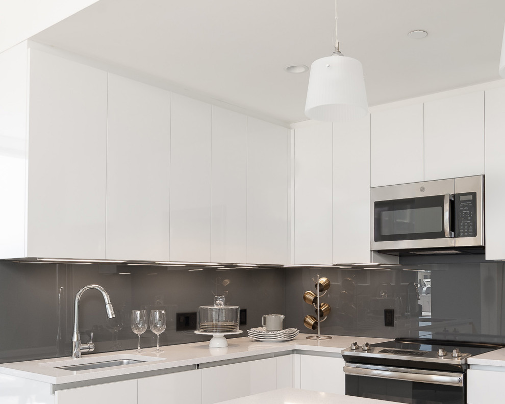 Modern inredning av ett mellanstort vit vitt kök, med en nedsänkt diskho, släta luckor, vita skåp, bänkskiva i onyx, grått stänkskydd, glaspanel som stänkskydd, rostfria vitvaror och en köksö